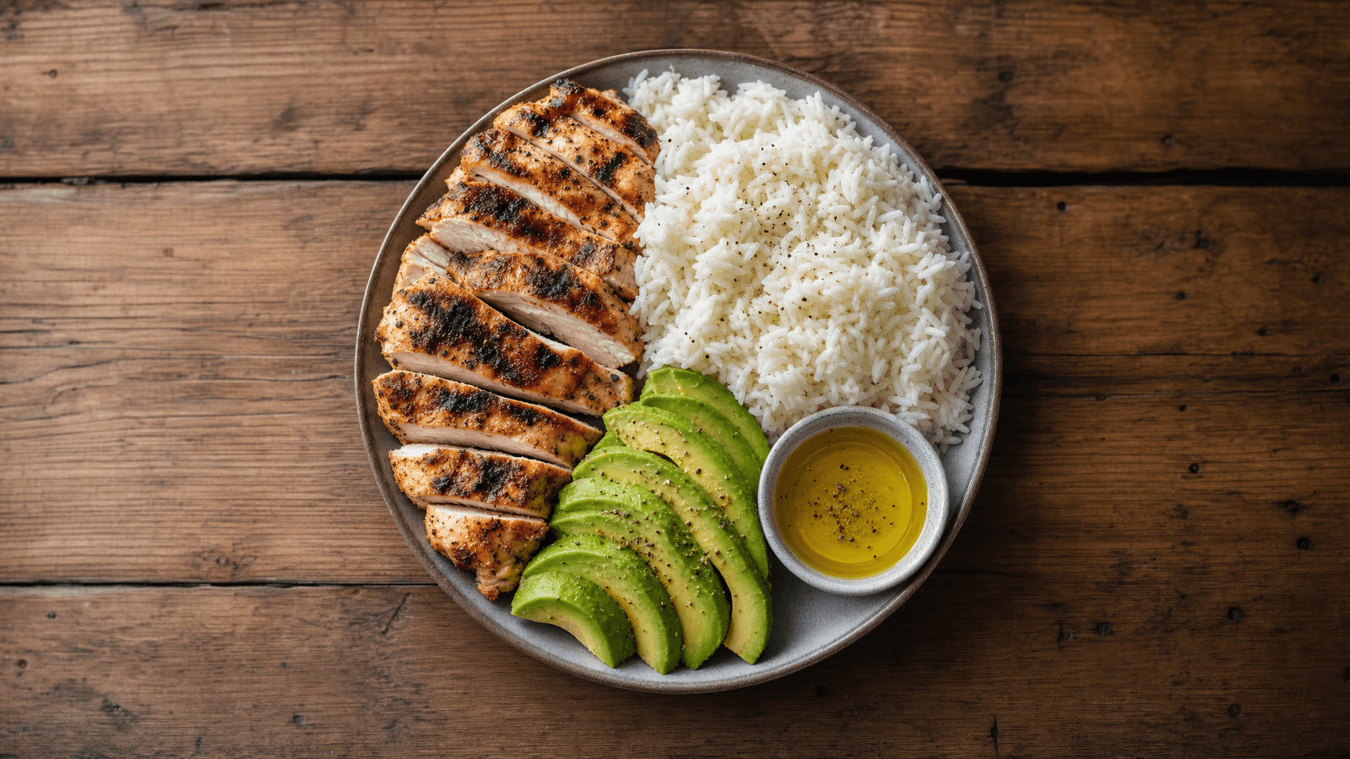 A plate divided into portions of grilled chicken, white rice and avocado representing a bulking macro split